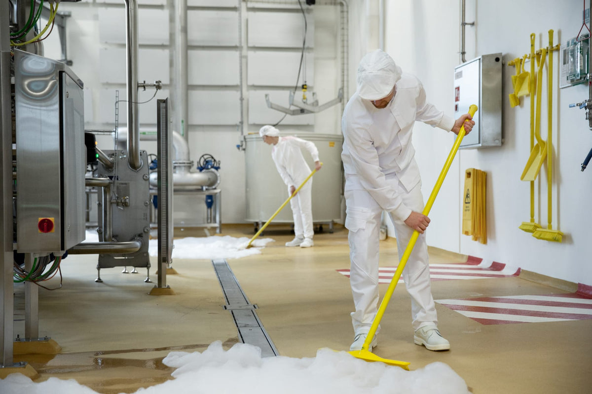 Mitarbeiter in weißer Hygienekleidung reinigen den Boden in einem Lebensmittelbetrieb