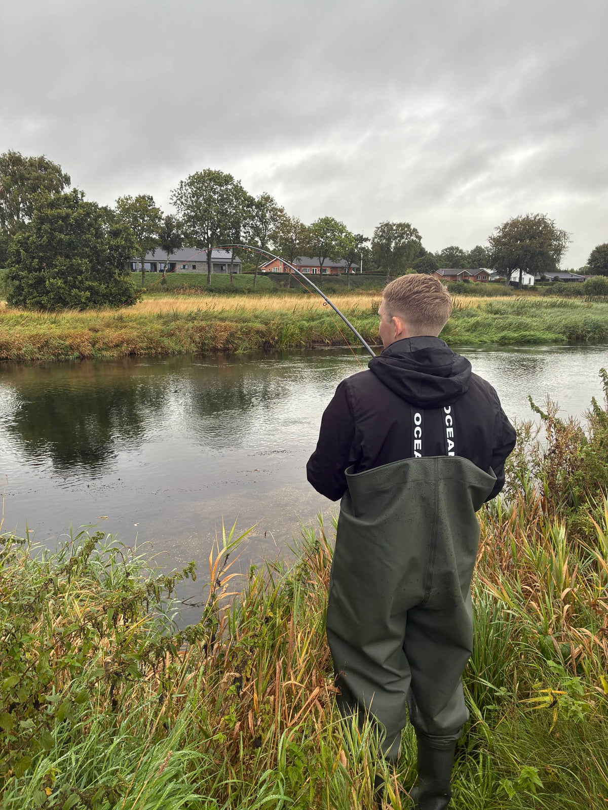 Angler in OCEAN-Wathose steht im Fluss in der Abenddämmerung