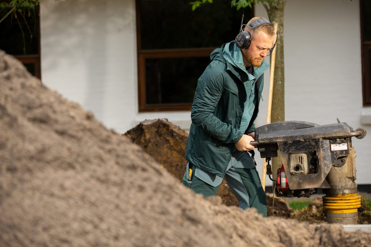 Landschaftsgärtner in grüner MASCOT-Arbeitsjacke mit Gehörschutz an einer Rüttelplatte
