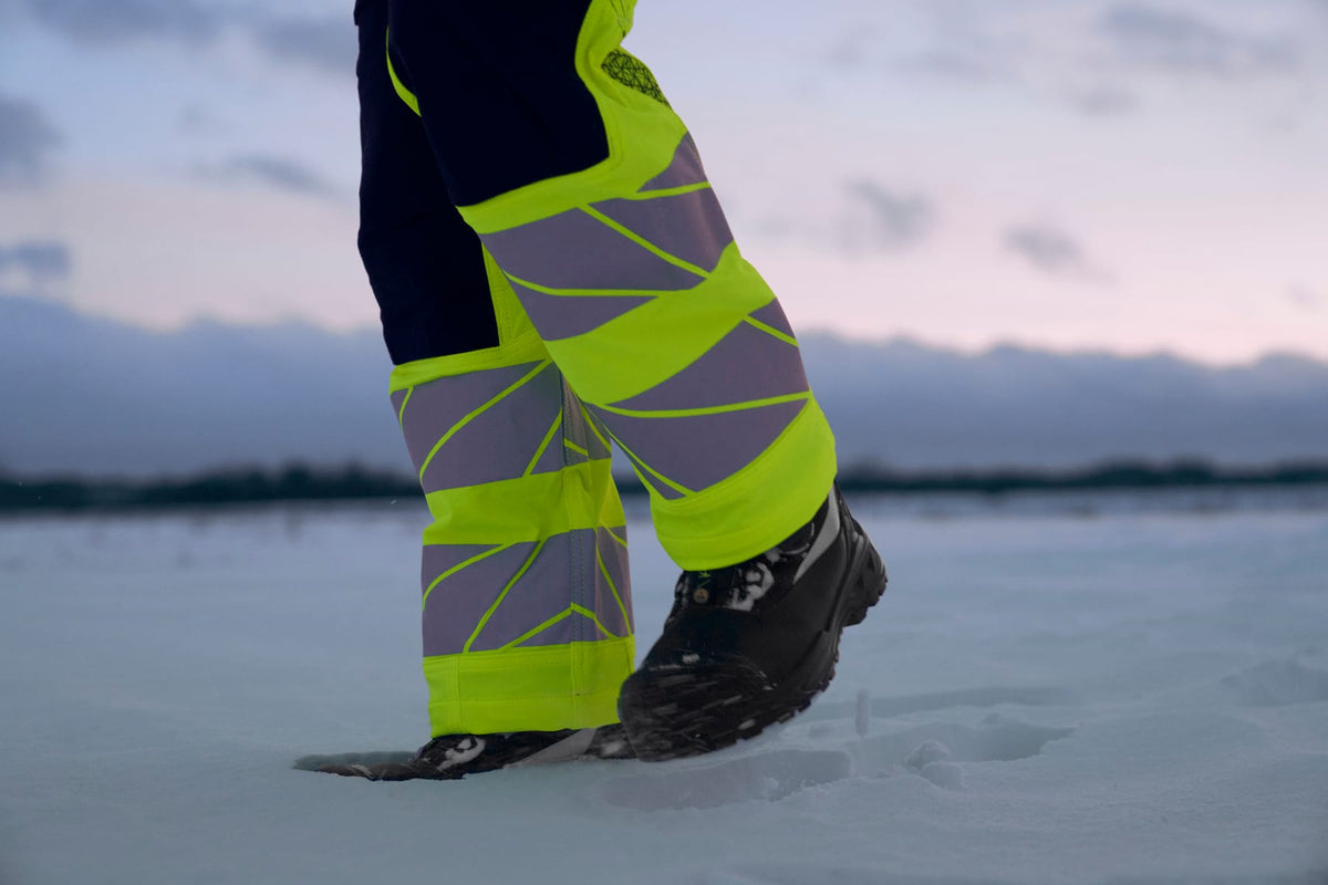 Gelbe MASCOT-Warnschutzhose mit Reflexstreifen und Winterstiefel im Schnee
