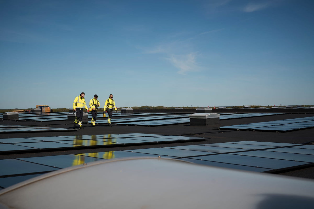 Drei Monteure in gelber MASCOT-Warnschutzkleidung auf einem Dach mit Solaranlage