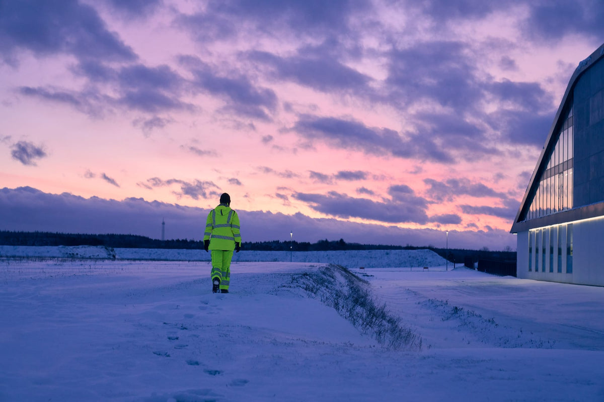 Person in gelber MASCOT-Warnschutzkleidung geht in der Abenddämmerung durch den Schnee